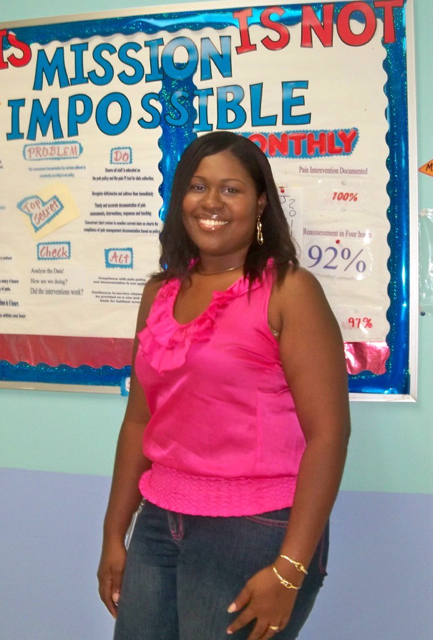 Shenequa Dore-Hamilton stands in front of an ER bulletin board she designed on giving excellent patient care. 
