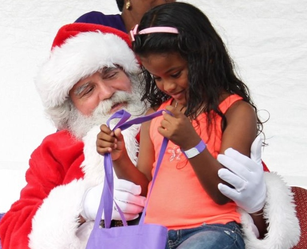 A little girl peeks into the goody bag Santa has just given her.
