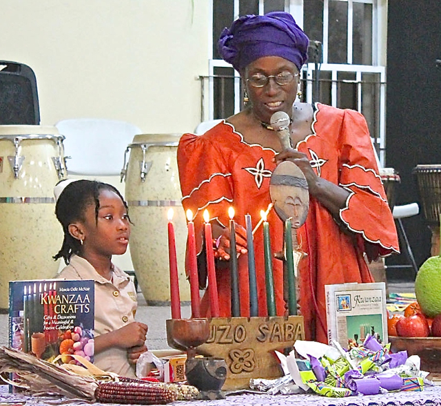 7-year-old Shenelle Bailey helps event organizer Jaribu Bobo light one of the seven Kwanzaa candles.