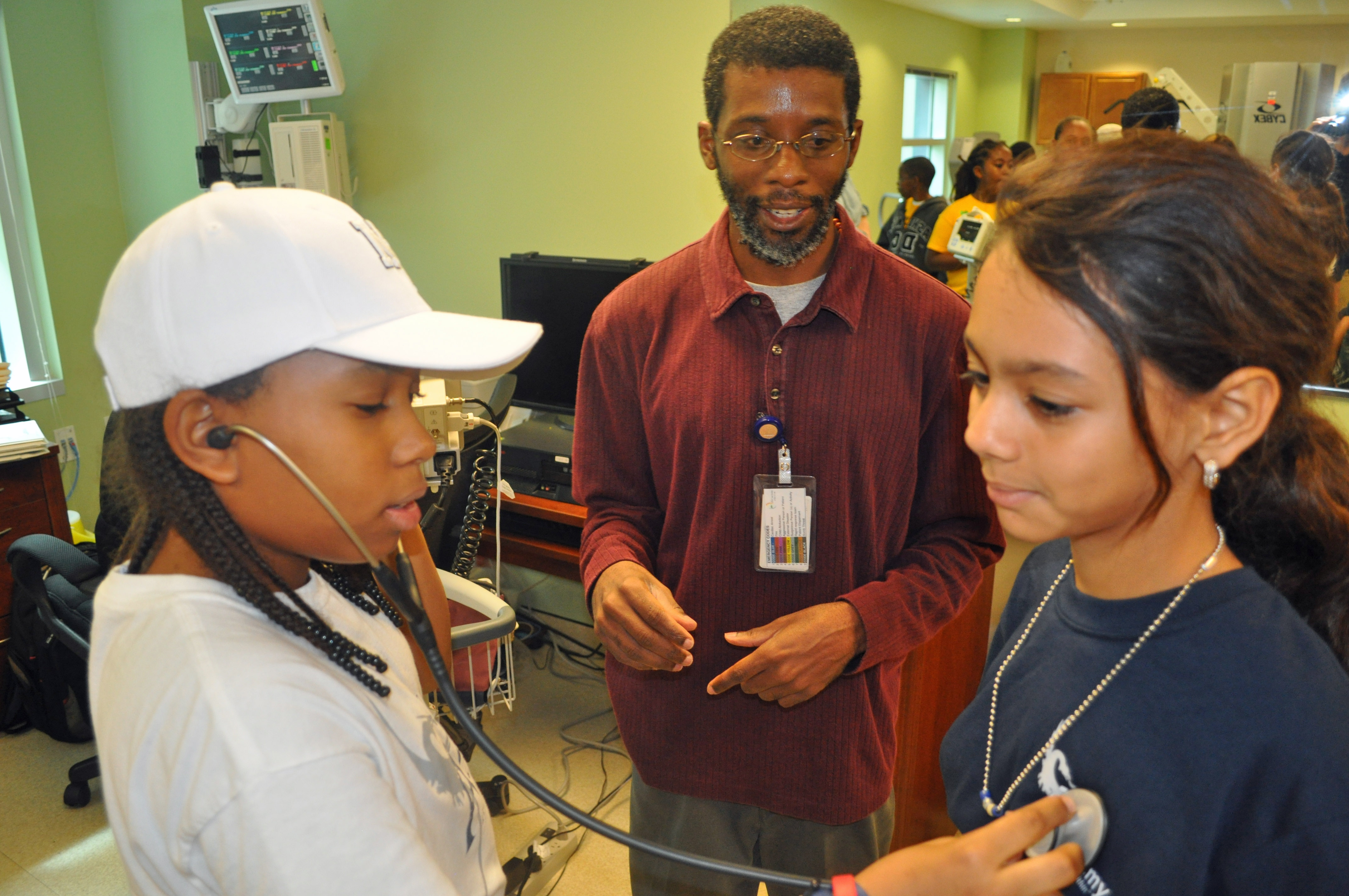 Exercise physiologist Andrew Edwards (center) shows Jesus Felix (left) how to use a stethoscope on fellow 6th grader Cayla Felix.