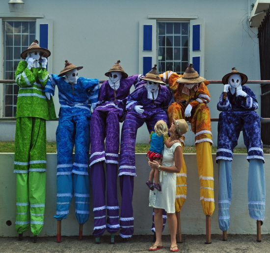 Mocko jumbies from the Ricardo Richards School take a load off and enthrall a girl and her mother.