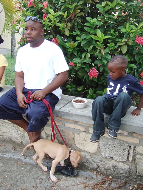 A puppy chews a shoe as its owners, Gustave Simmonds and Herman Marcus, 4, waitat Holy Cross.