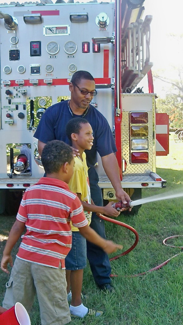 Firefighter George Otto helps 11-year-old Maki Edwards how to use the fire hose. 