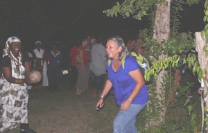 Before going to seek out jumbies, Veronica Gordon, smiling and holding calabash, has every member of the group pass through a low gate as a precaution.