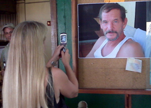 At Hull Bay, a woman takes a picture of a picture of Dennis Richardson, for whose Oct. 14 stabbing death two suspects pleaded not guilty Thursday in territorial court.