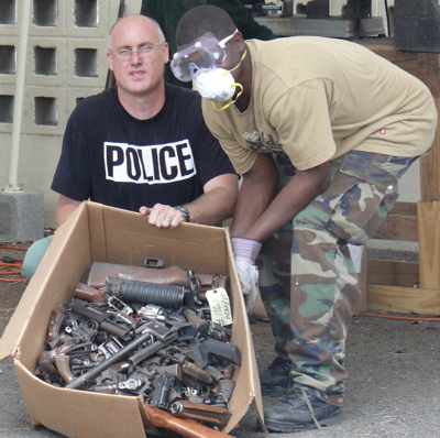 St. Croix Deputy Police Chief Chris Howell, left, and an officer masked by safety gear, with a box of weapons about to be destroyed.