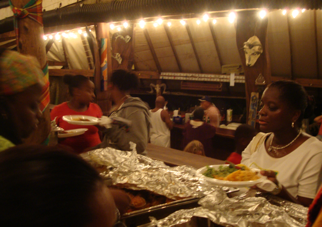 Carol Frank looks over the long table full of food at Jumbie Talk. She is served by Aminah Saleen, far left.