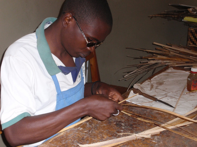 Blind and deaf, John cuts weaving material at the Ubumwe Community Center.