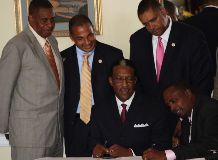 Sens. Louis P. Hill and Celestino A. White Sr. and Gov. John deJongh Jr. (top row from left) watch as V.I. Housing Authority head Robert Graham and V.I. Housing Finance Authority head Clifford Graham (bottom row from left) sign the transfer documents.
