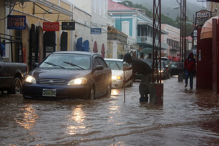 A good samaritan tries to unclog a gut on St. Thomas' Main Street as motorists move slowly up the submerged road.