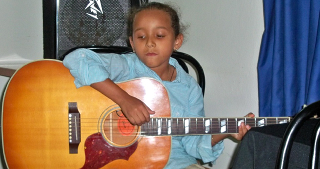Nathalia Samayoa, 7, is almost hidden behind the guitar she played Saturday at the Coffee House Fundraiser for Queen Louise Home.