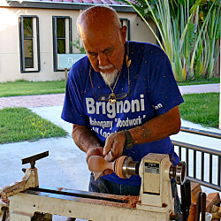 Dappled in wood chips and sawdust, Bien Brignoni turns a piece of mahogany on a lathe.