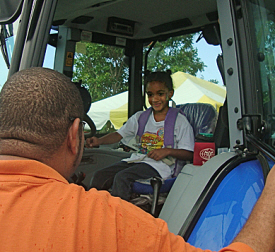 J Melendez of the V.I. Department of Agriculture helps 5-year-old Jaisha into the cab of a tractor.