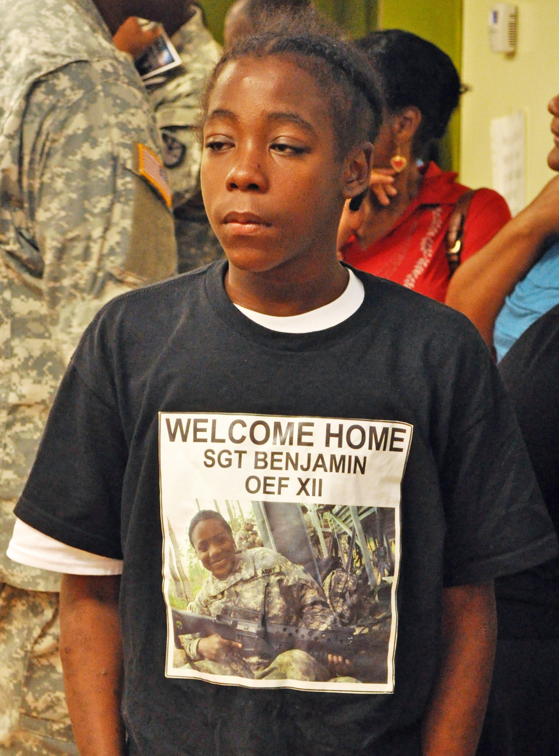 Joseph Harris, 15, waits to greet his sister, V.I. Guardswoman Asheba Benjamin. Seven members of Benjamin's welcoming party wore T-shirts the same as this one. The back read, "At Ease."