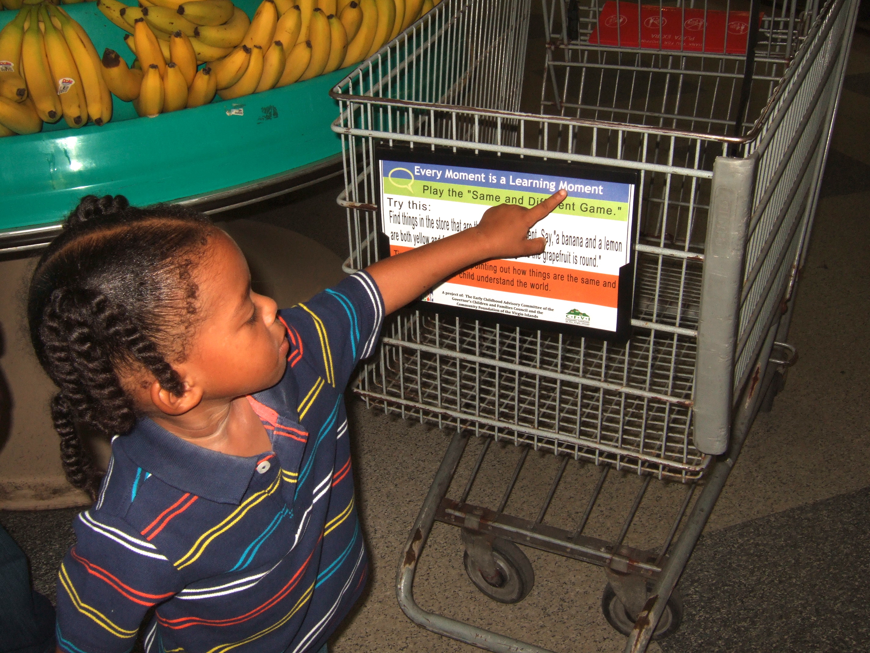 CFVI carts: Three-year-old L Trelle Nisbett points out the Everyday Moments are Learning Moments placard with games to play while shopping.