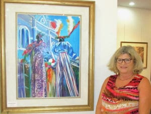 Melia Cook of the St. Thomas Historical Trust poses with Marsha Stein’s painting of mocko jumbies at the exhibition in Yacht Haven Grand. It will be open through Saturday.