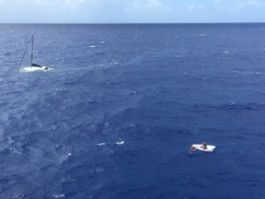 Robert Petersen of St. Thomas sits in his life raft as a Coast Guard rescue swimmer talks to him Friday, with the sunken 36-foot sailing vessel Wings in the background, about six miles southwest of Big Sand Cay in the Turks and Caicos. (U.S. Coast Guard photo)
