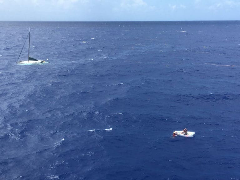 Robert Petersen of St. Thomas sits in his life raft as a Coast Guard rescue swimmer talks to him Friday, with the sunken 36-foot sailing vessel Wings in the background, about six miles southwest of Big Sand Cay in the Turks and Caicos. (U.S. Coast Guard photo)