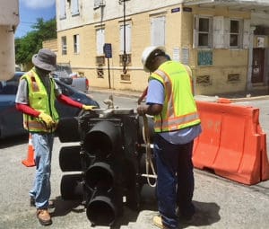 Two Department of Public Works employees prepare a new traffic light to hang over an intersection.