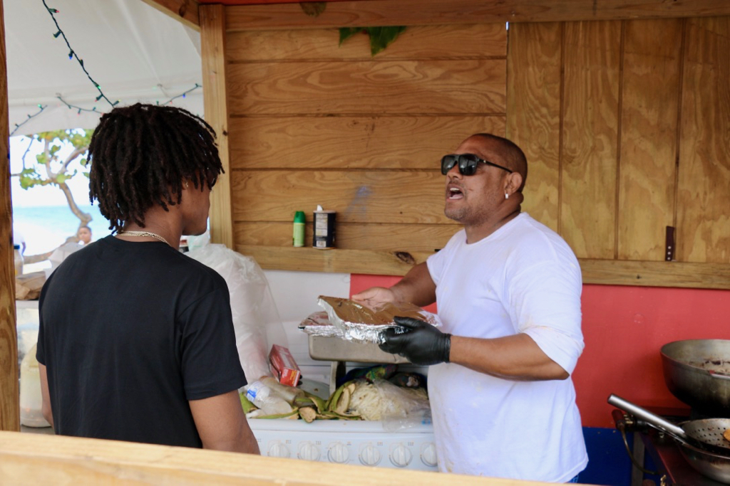 Israel Contreras, busy in the cook tent, gives instructions to one of the campers to pick up any trash on the beach. Passionate about keeping Little Bay clean, Contreras said the campers clean up morning and evening. (Linda Morland photo)
