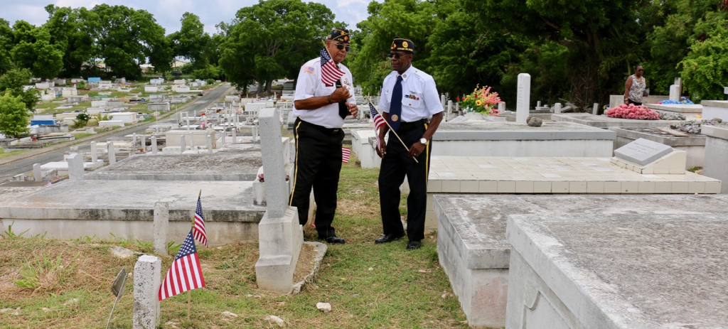 Bruce Gordon, 1St. Vice Commander and Ira Williams, 2nd Vice Commander of American Legion Enrique Romero Nieves Post No. 102 examine the new flags being placed on the graves of veterans in the Kingshill Cemetery. (Linda Morland photo)