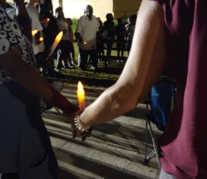 Community members hold hands and candles in remembrance of those who have died violently in their community. (Source photo by Shaun Pennington)