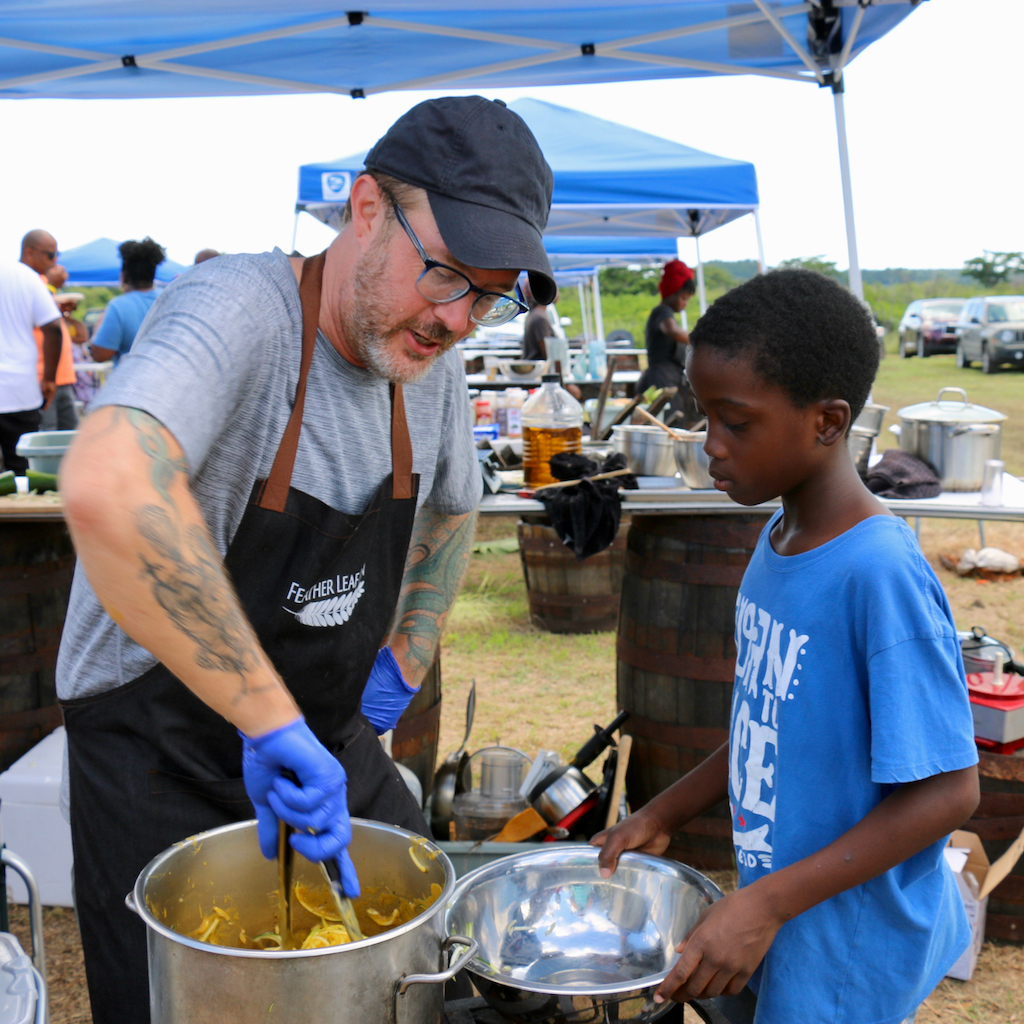 Sugar Apple chef Blake Gardner stirs a pot as Micah Paul, aged 8 assists. Micah says he has already decided to become a chef. (Source photo by Linda Morland)