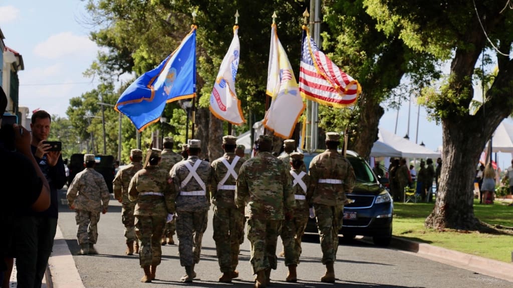 Banners wave in the wind as the Army National Guard marches down Strand Street. (Source photo by Linda Morland)