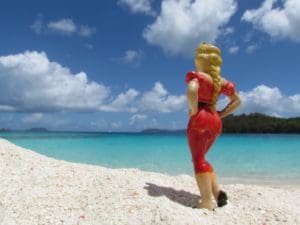 Image from 'On These Shores' – photograph of figurine in red dress on the beach, by Janet Cook-Rutnik. (Submitted photo)