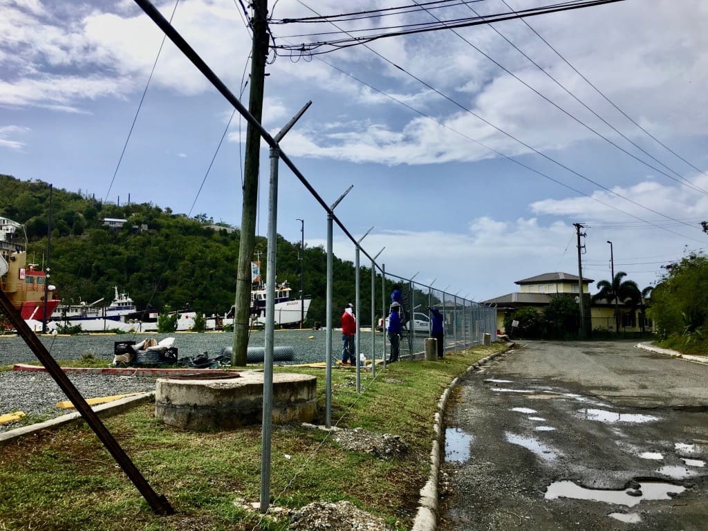 A construction crew installs fencing around the lot. Rain fills potholes on Fish Fry Road. Residents have complained that the road floods more often since the parking lot was installed. (Source photo by Amy Roberts)