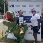 Amy DeSorbo, Director of Division of Libraries, Archives and Museum (DPNR) in a dinosaur costume takes photo with Cusa Holloway, Incubator Program Manager , VIEDA at the 2022 AgFair in St. Croix