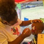 Shaka, 4 years old, gets a Spiderman facepainting by young artist at the Child’s Party Service booth.