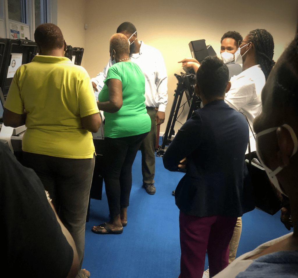 Lt. Governor candidate Janelle Sarauw (on the right in white shirt) asks a question about how tabulators tell users if their ballot has been spoiled. Demonstrators said the tabulator would display a notice on the screen before accepting the ballot. If the voter chose to submit the ballot after seeing the notice, the portion with the uncorrected defect would be counted as spoiled. (Photo by Judi Shimel)