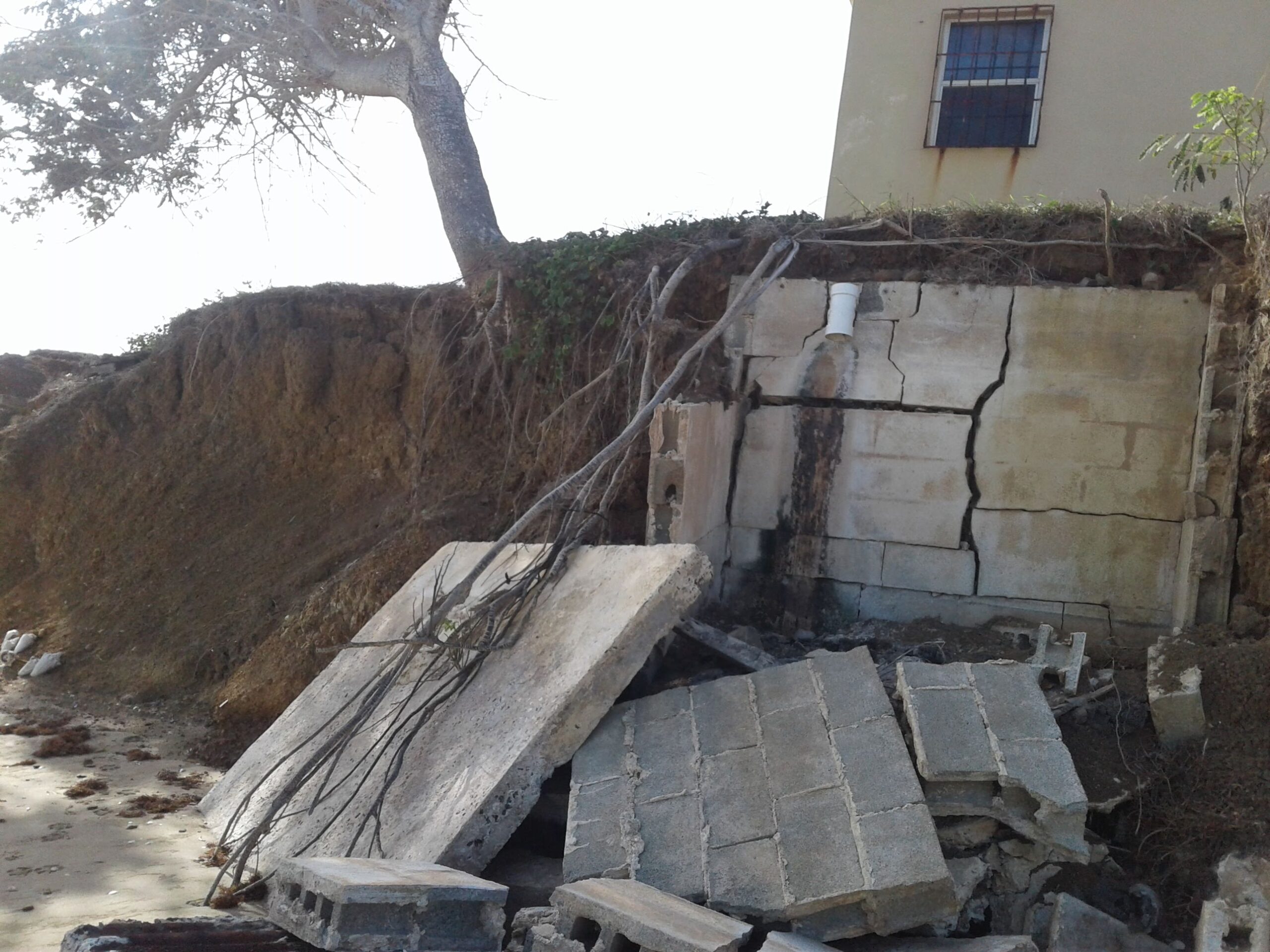 Due to erosion, a house’s septic tank has been washed into the ocean. The house is about to fall into the sea, as well. (Photo by Olasee Davis)