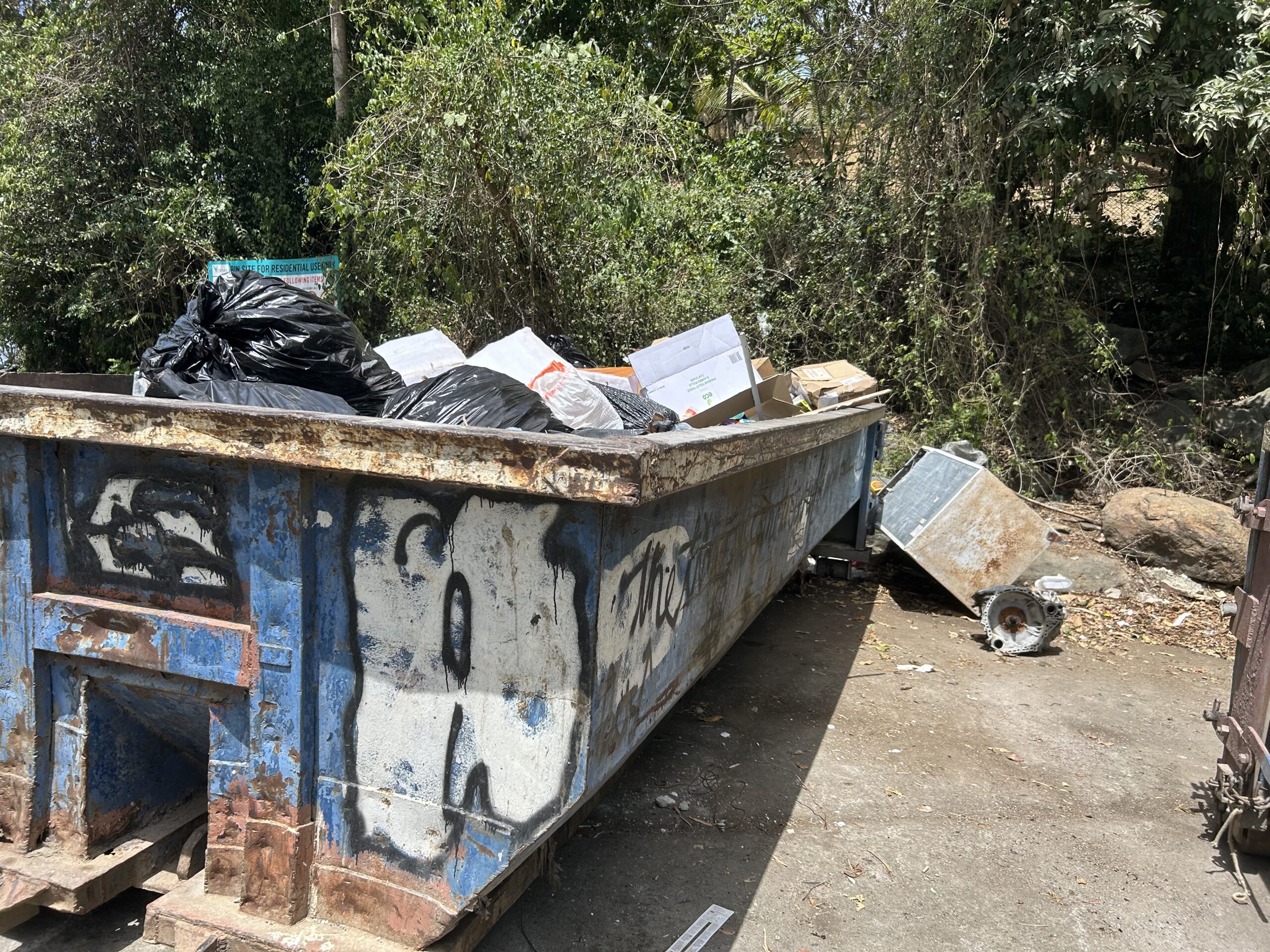 A small fridge and what appears to be an engine part lie next to the dumpster at Caret Bay on St. Thomas. (Source photo by Siรขn Cobb)